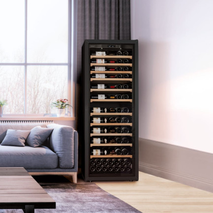 Large wine cabinet with glass door and free-standing black frame in a living room next to the sofa - La Première EuroCave Large wine cabinet with glass door and free-standing black frame in a living room next to the sofa - La Première EuroCave