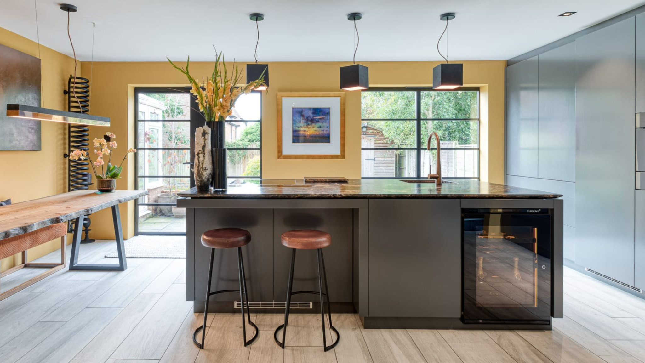 Small glazed service wine cooler, amber lighting, set in a central island of a fitted kitchen in wood and gray colours. Small glazed service wine cooler, amber lighting, set in a central island of a fitted kitchen in wood and gray colours.