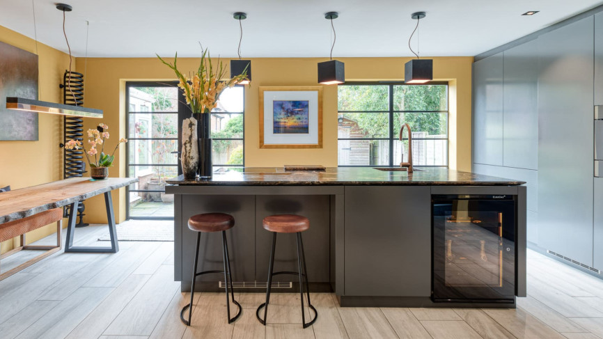 Small glazed service wine cooler, amber lighting, set in a central island of a fitted kitchen in wood and gray colours. Small glazed service wine cooler, amber lighting, set in a central island of a fitted kitchen in wood and gray colours.